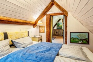 A bedroom with a sloped ceiling, a bed with white and blue bedding, a nightstand, and a painting on the wall. - Holiday apartment House of the Painters' Cloud Two (Müllheim)