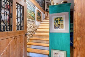 A wooden staircase with a stone wall on one side and a teal cabinet with framed artwork. - Holiday apartment House of the Painters' Cloud Two (Müllheim)