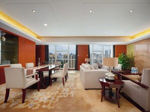 Habitación de hotel con zona de comedor, sofá, mesita de centro y un amplio ventanal con vista a la ciudad.