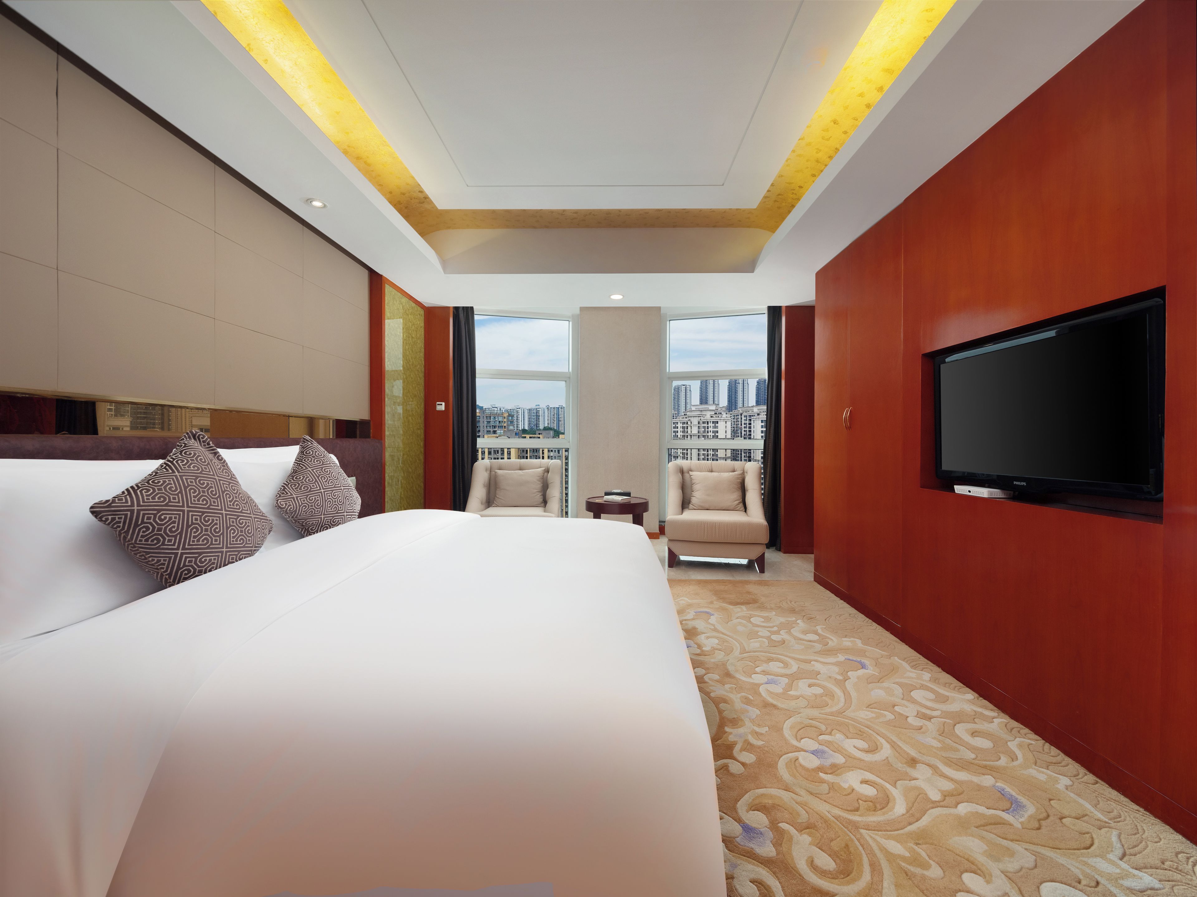 A hotel room with a large bed, a television, a chair, and a view of the cityscape.