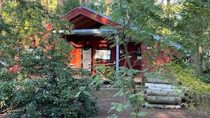 Uma cabana com fachada vermelha, rodeada por uma floresta densa.
