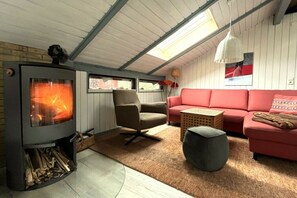 A cozy living room with a wood-burning stove, a red sofa, a brown armchair, and a round ottoman. - Holiday home Wendland hideaway (Gartow)