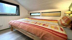 Quarto com uma cama de solteiro, duas janelas, um radiador e uma luminária na mesa de cabeceira.