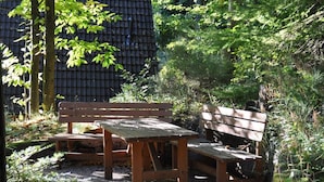Ein Holzbänkchen und Tisch in einem Garten mit dichtem Grünwerk und einer Steinmauer im Hintergrund.