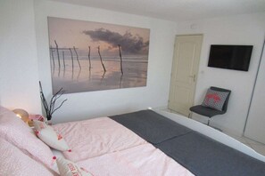 A bedroom with a bed, a wall-mounted TV, a door, and a chair. - La Baie du Levant 12 (Gruissan)