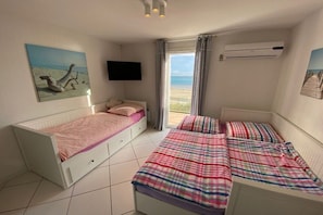Een slaapkamer met twee bedden, een televisie en uitzicht op het strand.