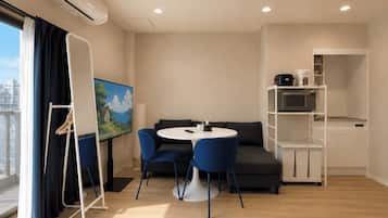 Habitación moderna con una mesa redonda, sillas azules, un sofá, un televisor de pantalla plana y una kitchenette.