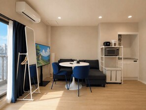 A modern room with a round table, blue chairs, a sofa, a flat-screen TV, and a kitchenette. - SOL Guesthouse Konohana (Osaka)