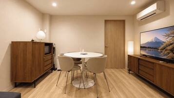 A compact room with a round table, two chairs, a television, and a cabinet with a lamp.