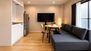A modern living space with a sofa, a dining table, a flat-screen TV, and a kitchen area.