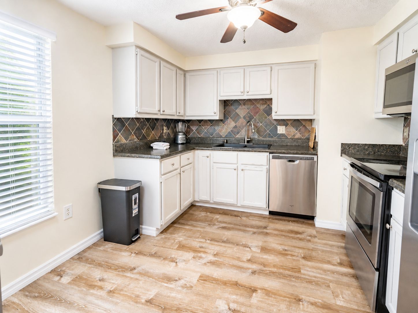 A kitchen with white cabinets, a tiled backsplash, a dishwasher, and a stove.