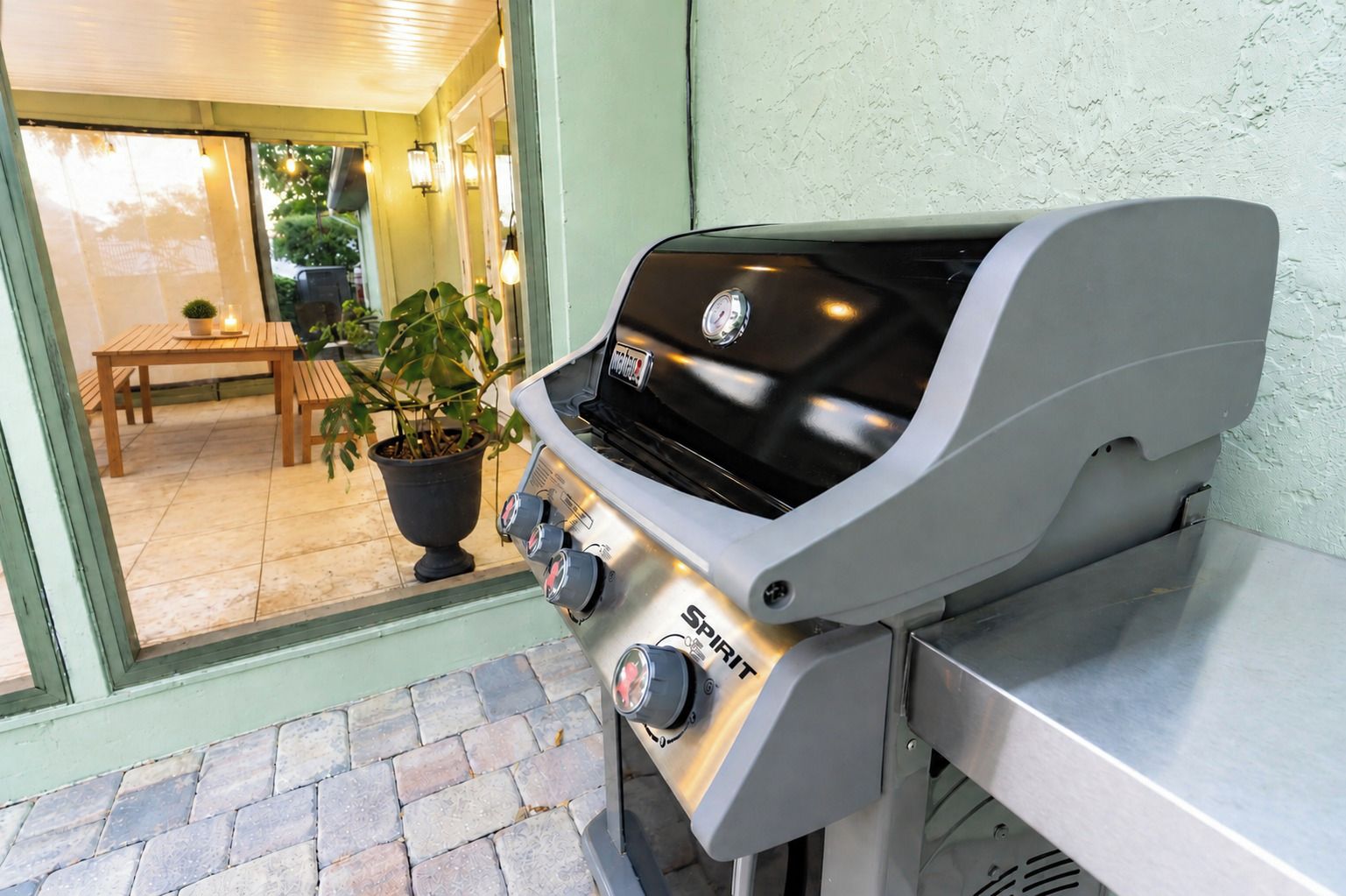 An outdoor grill with a control panel, a potted plant, and a wooden bench.