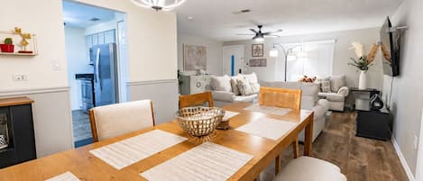 A modern living room with a dining area, a kitchen in the background, and a ceiling fan.