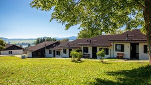 A row of houses with a grassy lawn in front, a clear sky, and distant hills. - Holiday home "Hochplatte" (Lechbruck)