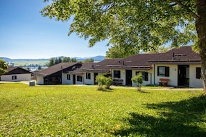 Fileira de casas com gramado à frente, céu claro e colinas ao longe.