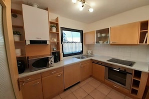 A compact kitchen with a microwave, oven, sink, and wooden cabinets. - Holiday home "Hochplatte" (Lechbruck)