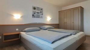 A bedroom with a bed, bedside tables, a wardrobe, and wall-mounted lights. - Holiday home "Hochplatte" (Lechbruck)