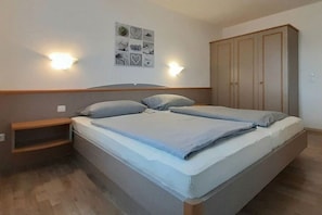Quarto com cama, mesas de cabeceira, guarda-roupa e luminárias na parede.