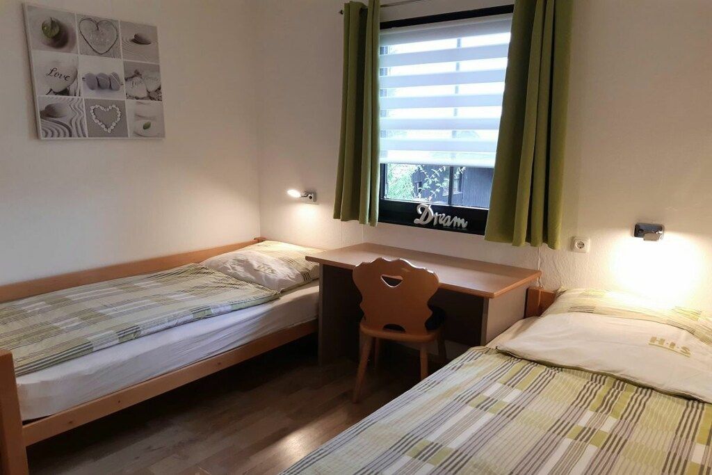 Een kleine, eenvoudige kamer met twee eenpersoonsbedden, een bureau en een stoel.
