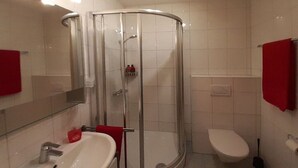 A bathroom with a glass-enclosed shower, a white sink, a toilet, and a red towel. - Holiday home "Hochplatte" (Lechbruck)