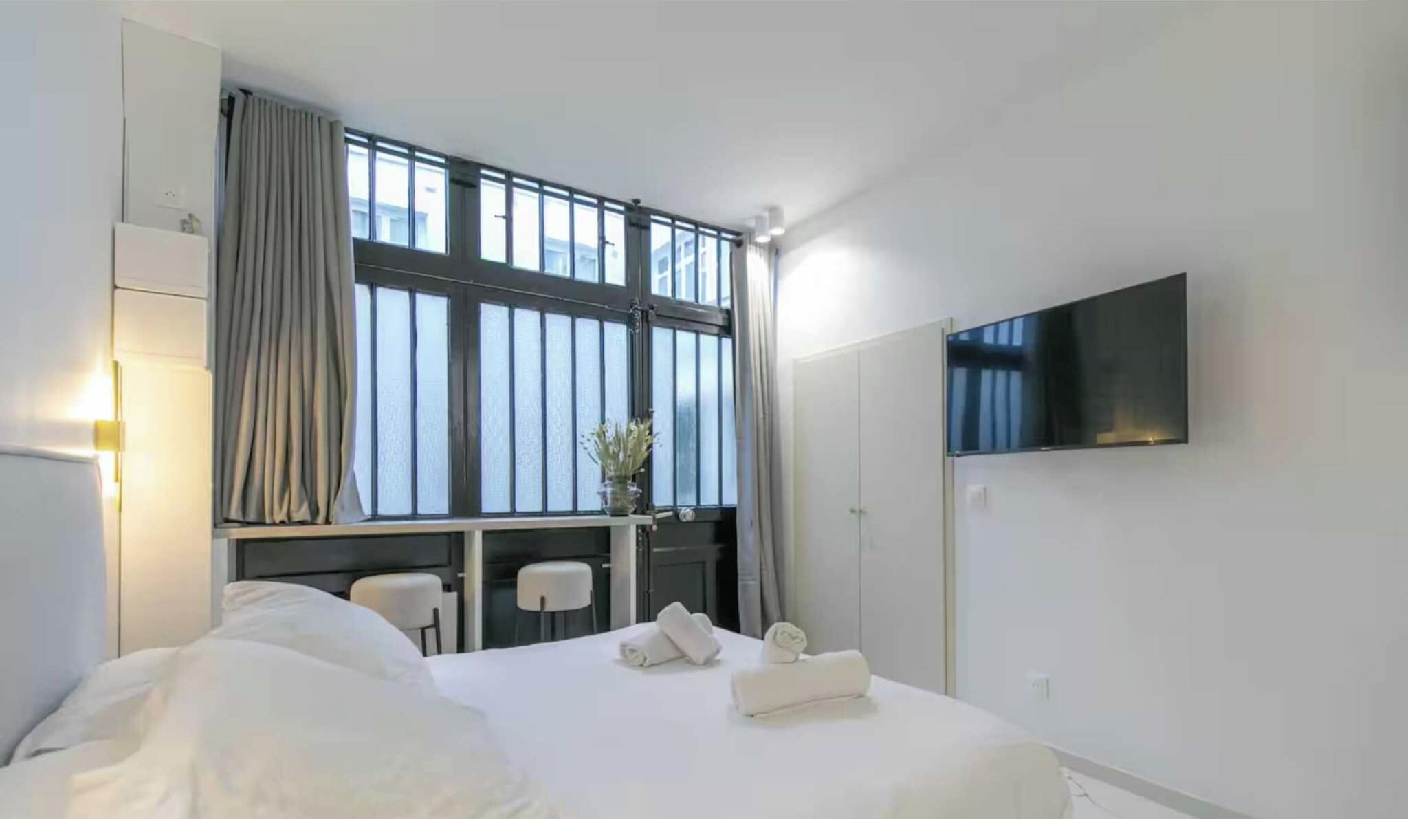 A hotel room with a bed, a desk, a chair, a TV, and a window with curtains.