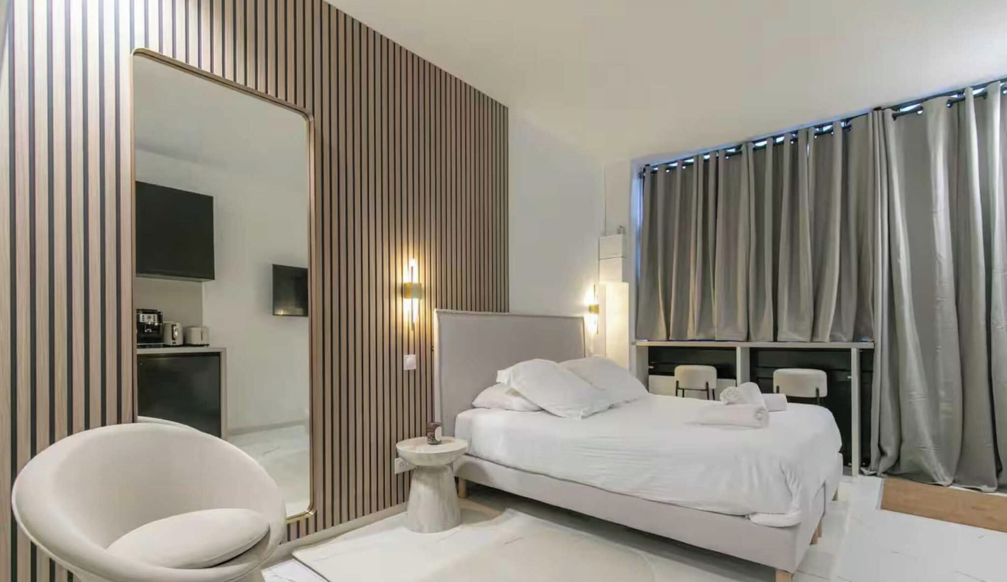 A modern bedroom with a large bed, bedside tables, a chair, a mirror, and curtains.