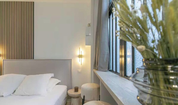 A hotel room with a bed, bedside table, lamp, and a window with a view. - Charming studio - 2P - Gare de l'Est (Paris)
