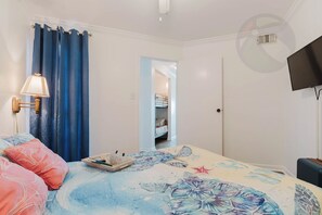 A bedroom with a bed, a bedside table, a lamp, a TV, and a wardrobe. - Tidal Treasure at the Victorian (Galveston)