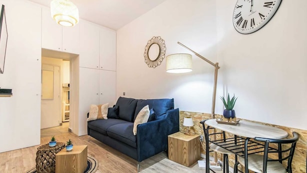 Een moderne woonkamer met een bank, een eettafel met stoelen, een lamp, een klok en een plant in een pot.