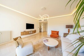 Ein modernes Wohnzimmer mit Fernseher, einem weißen Sofa, einem orangefarbenen Sessel und einem Couchtisch.