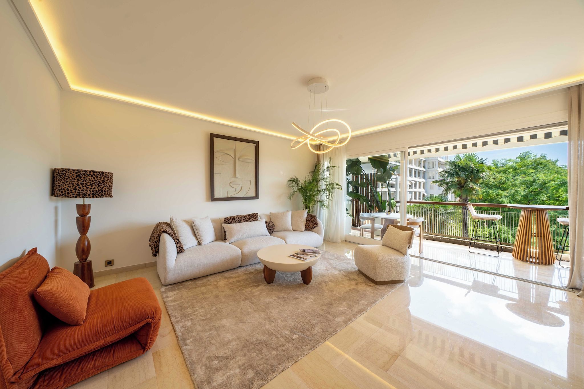 A modern living room with a sofa, armchairs, a coffee table, and a balcony with outdoor furniture.
