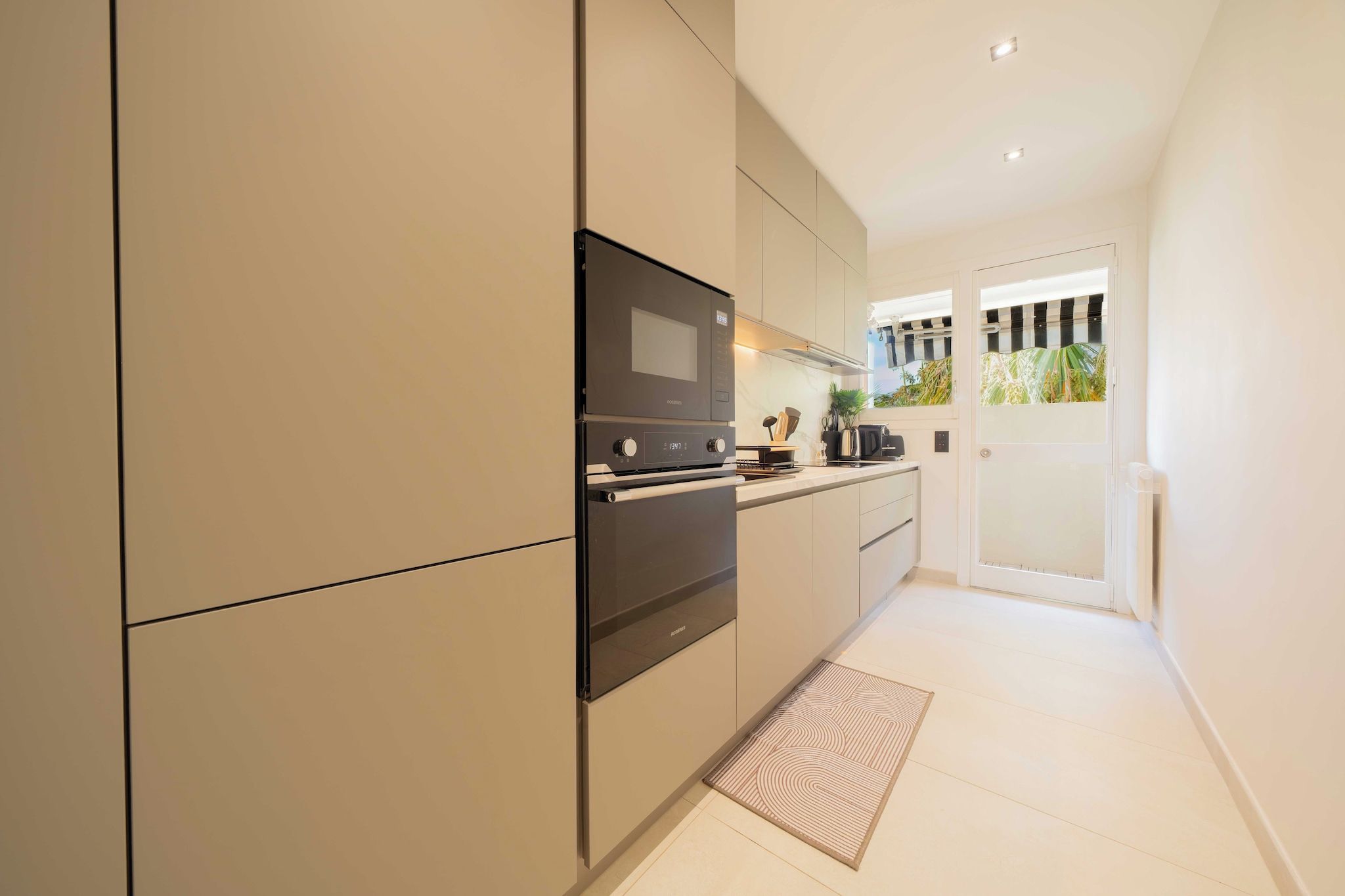 A modern kitchen with built-in appliances, a small countertop, and a view of a balcony with plants.