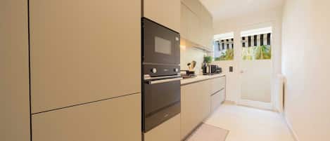 A modern kitchen with built-in appliances, a small countertop, and a view of a balcony with plants.