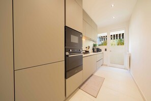 Une cuisine moderne dotée d’appareils électroménagers intégrés, d’un petit plan de travail et offrant une vue sur un balcon agrémenté de plantes.