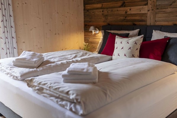 A neatly made bed with white linens and folded towels, a wooden headboard, and a wall-mounted lamp. - Apartment with 1 bedroom (St. Georgen am Kreischberg)