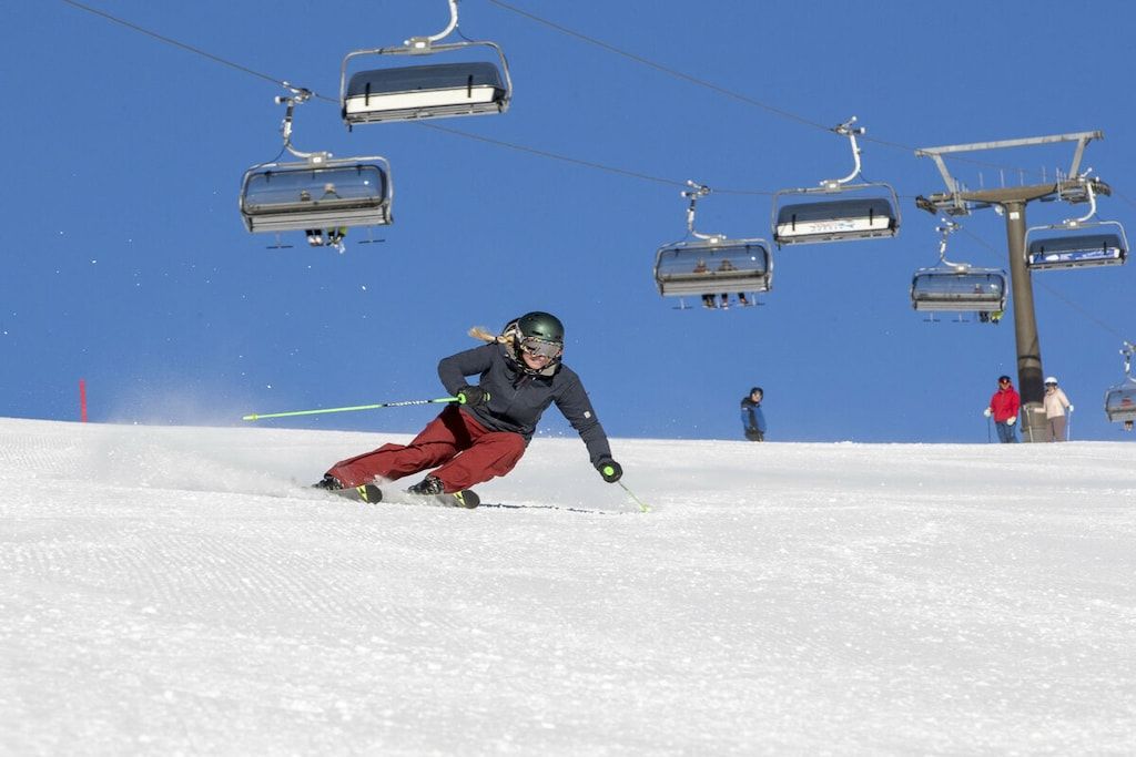 Une personne qui fait du ski sur une pente, avec des télésièges en arrière-plan.