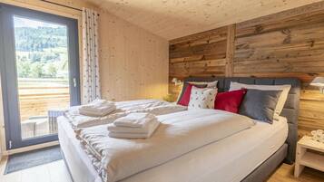 A bedroom with a large bed, a wooden headboard, and a view of a mountainous landscape through a sliding door.