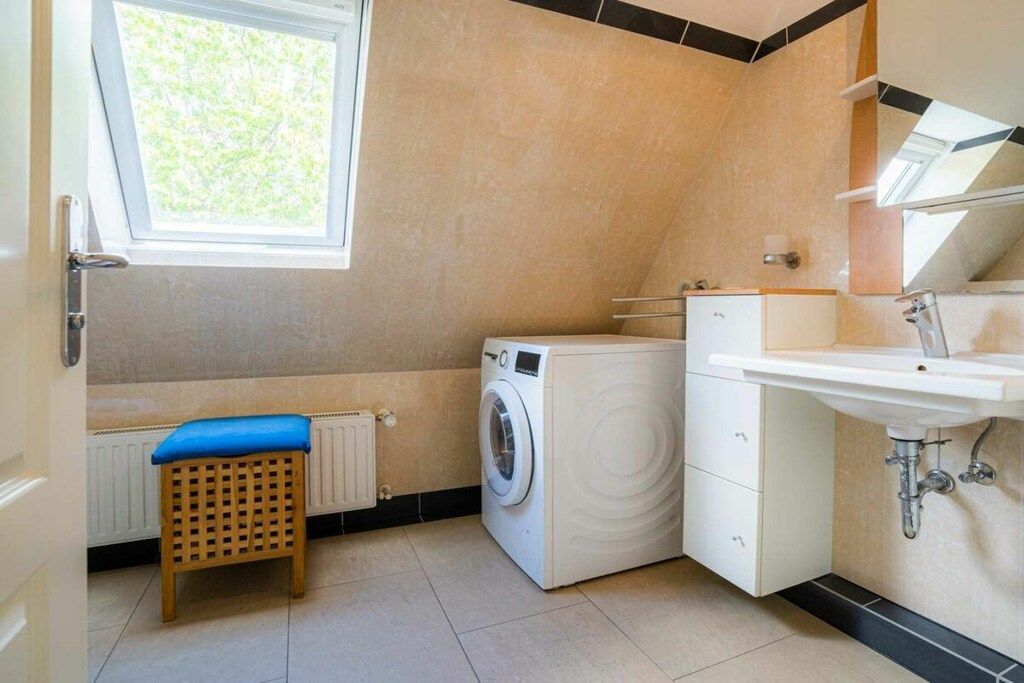 A compact laundry room with a washing machine, a small stool, a radiator, and a sink.