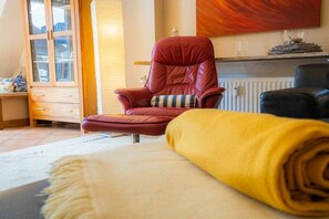 Een kamer met een rode lederen fauteuil, een gele opgerolde deken en een houten kast met glazen deuren.