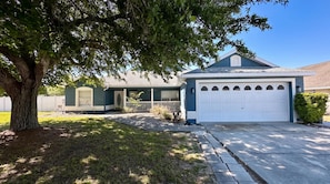 A residential house with a garage, a driveway, and a large tree in the front yard. - Starlight and Shells Pool (Davenport)