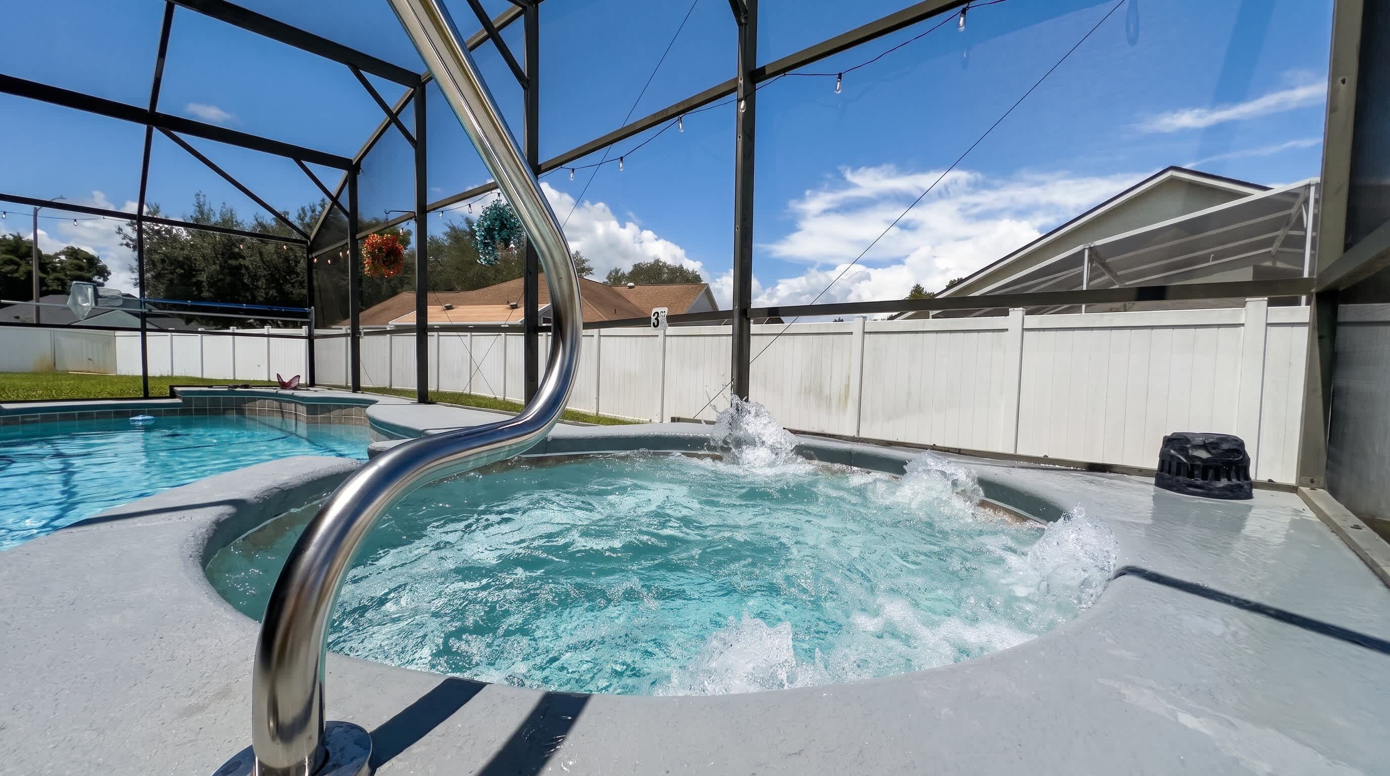 Un bain à remous avec un escalier en métal, entouré d’une clôture blanche et sous un ciel dégagé.