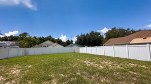 A backyard with a white fence, a grassy lawn, and houses in the background. - Starlight and Shells Pool (Davenport)