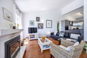 A living room with a fireplace, a television, a sofa, and a kitchen area.