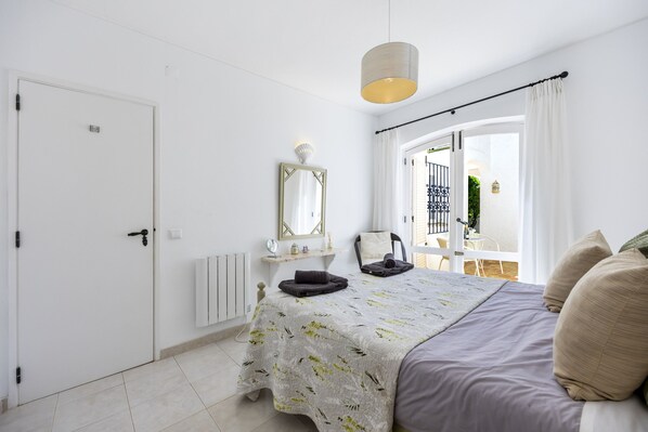 Une chambre à coucher avec un lit, une table de chevet, un miroir, une fenêtre avec des rideaux et une porte.