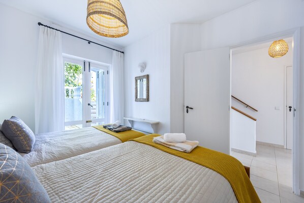 A hotel room with two beds, a window with curtains, a door, and a wall-mounted mirror.
