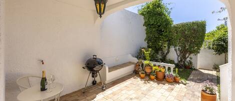 A patio with a grill, a table with chairs, and potted plants.