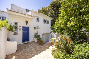 A white building with a blue door, potted plants, and a tiled courtyard.