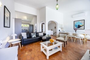 Un salon moderne avec un canapé en cuir noir, une table basse blanche et un coin repas comprenant une table et des chaises blanches.
