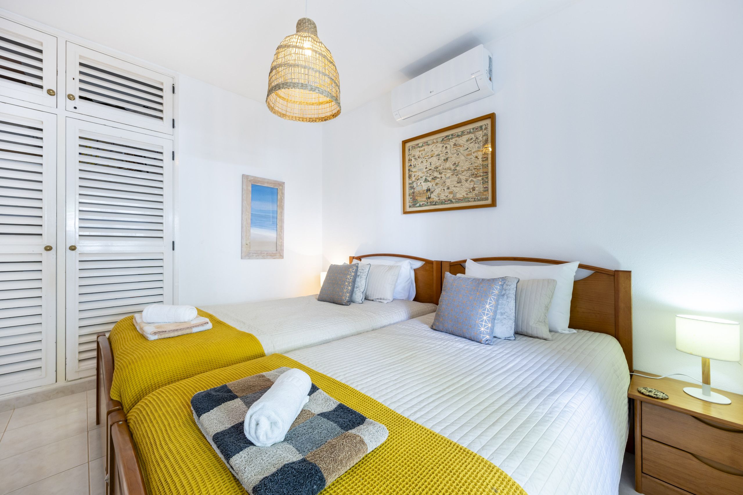 Habitació d'hotel amb dos llits, un penjador d'il·luminació, un aparell d'aire condicionat i un mapa emmarcat a la paret.