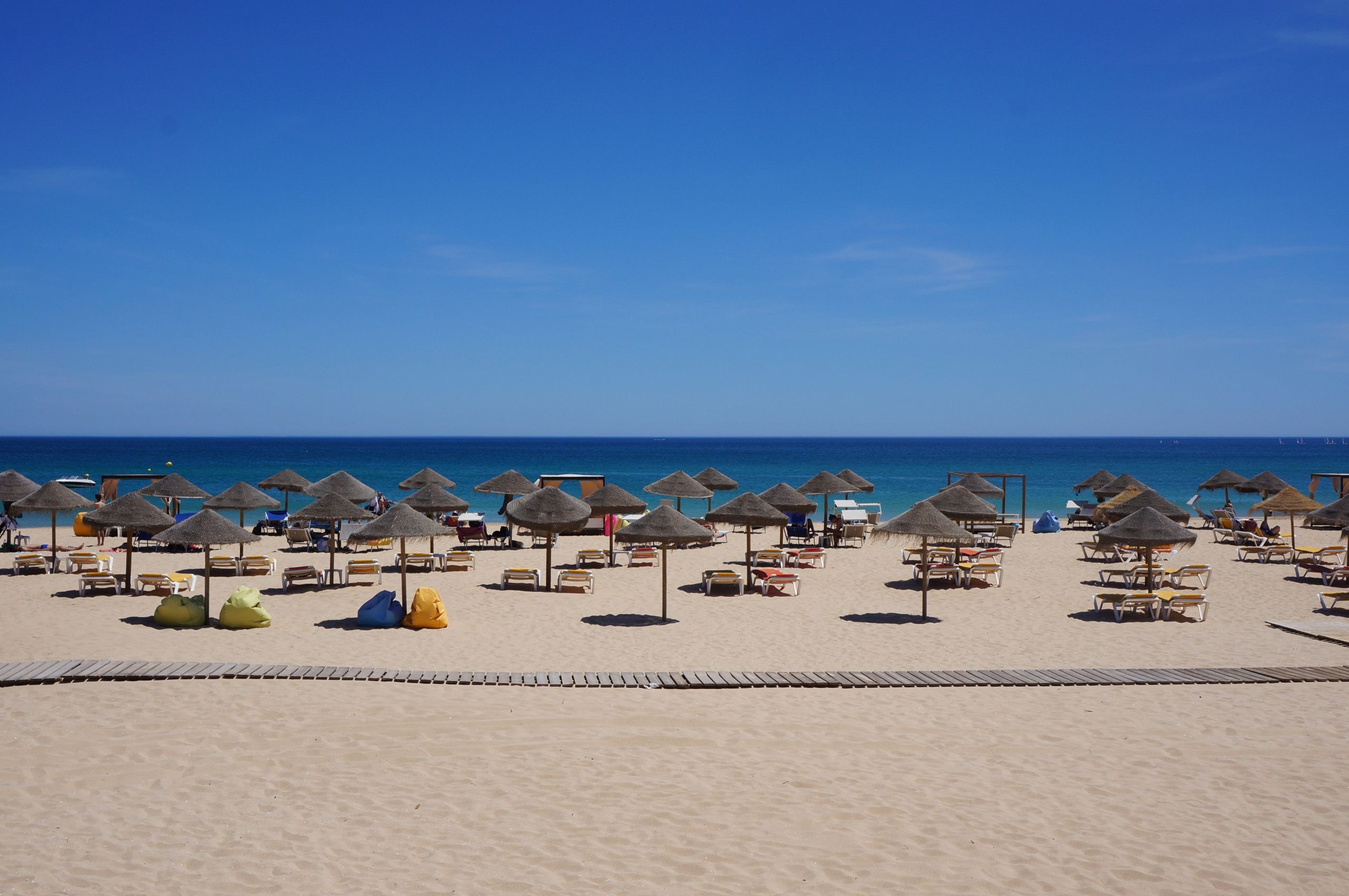 Une plage bordée de rangées de chaises longues et d’ombrelles en chaume, une promenade en bois et l’océan en toile de fond.